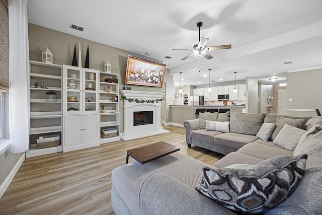 living area with light wood-style floors, baseboards, visible vents, and a fireplace with raised hearth