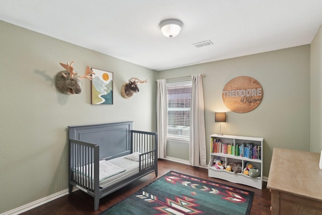 bedroom with a nursery area, wood finished floors, visible vents, and baseboards