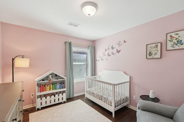 bedroom with dark wood-style floors, a nursery area, visible vents, and baseboards