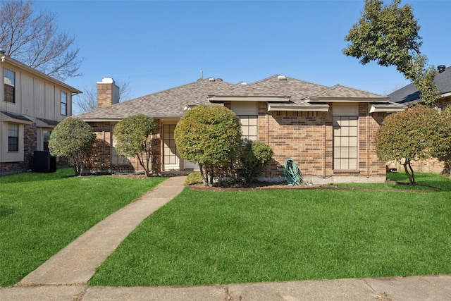 view of front of home with central AC unit, brick siding, roof with shingles, a chimney, and a front yard