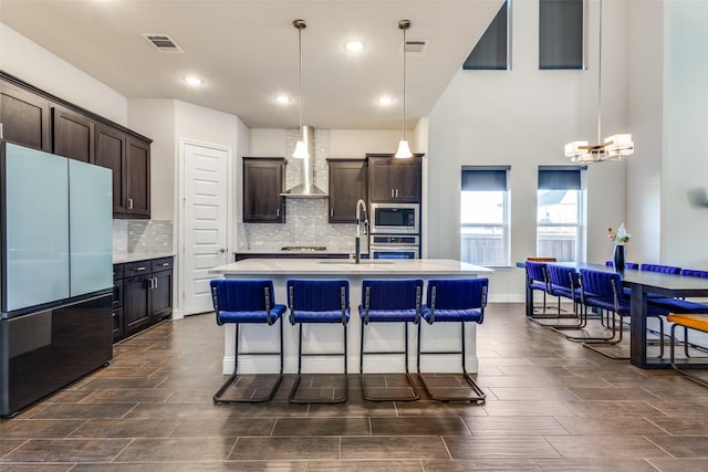 kitchen featuring stainless steel appliances, a sink, visible vents, light countertops, and wall chimney exhaust hood