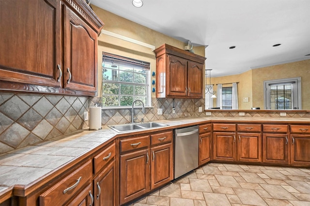 kitchen featuring tile countertops, a sink, stainless steel dishwasher, stone finish flooring, and tasteful backsplash