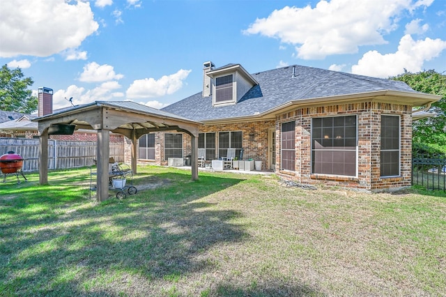 rear view of property featuring a patio, brick siding, fence, a lawn, and roof with shingles