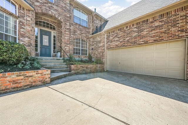 view of exterior entry featuring concrete driveway, brick siding, and roof with shingles