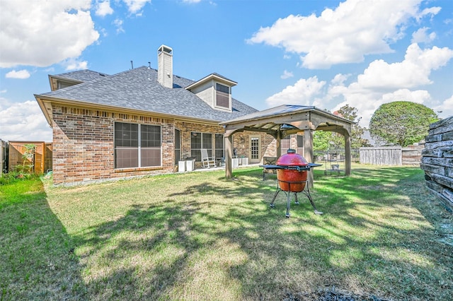 rear view of property with brick siding, fence, a gazebo, and a lawn