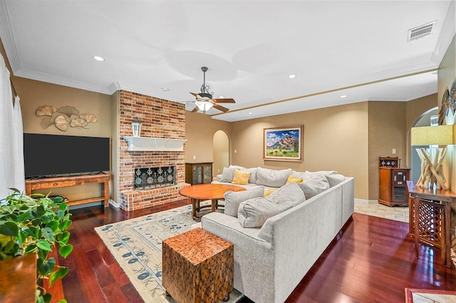 living room featuring arched walkways, hardwood / wood-style flooring, visible vents, a brick fireplace, and crown molding