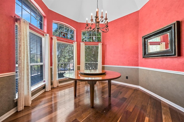 unfurnished dining area with baseboards, high vaulted ceiling, wood finished floors, and an inviting chandelier