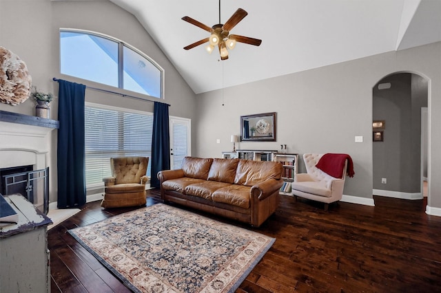 living area featuring baseboards, arched walkways, a fireplace with raised hearth, a ceiling fan, and wood-type flooring