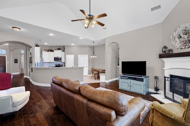 living area with dark wood-style floors, visible vents, arched walkways, and a fireplace with raised hearth