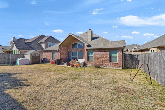 rear view of property featuring brick siding, a lawn, a shed, a fenced backyard, and an outdoor structure