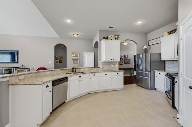 kitchen featuring light stone counters, stainless steel appliances, white cabinets, a sink, and a peninsula