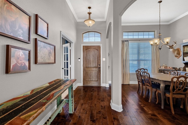 foyer entrance with arched walkways, a notable chandelier, dark wood-style flooring, baseboards, and crown molding