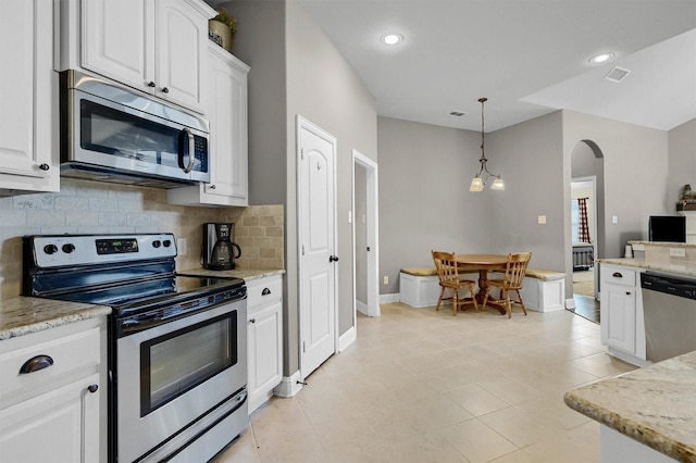 kitchen featuring arched walkways, white cabinetry, appliances with stainless steel finishes, decorative backsplash, and decorative light fixtures