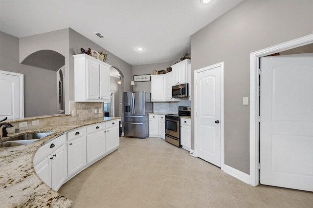 kitchen with visible vents, light stone countertops, stainless steel appliances, white cabinetry, and a sink