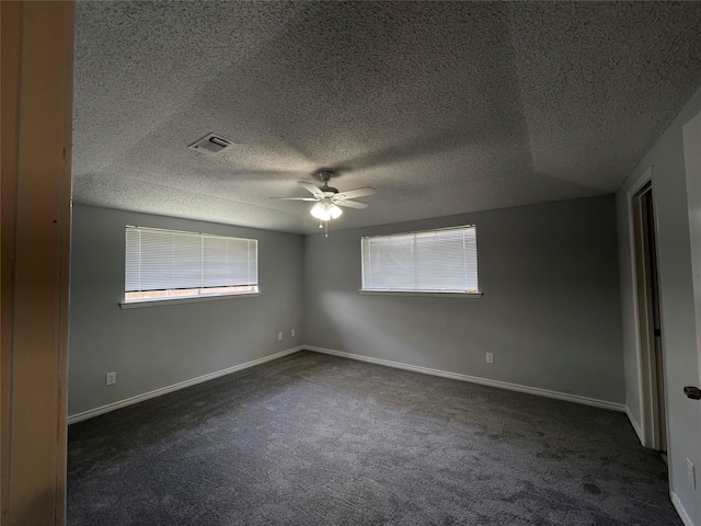 empty room featuring dark colored carpet, visible vents, ceiling fan, and baseboards