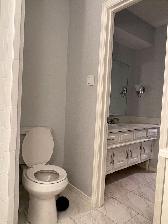 bathroom featuring toilet, marble finish floor, baseboards, and vanity