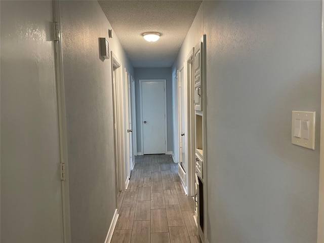 hall with a textured wall, baseboards, a textured ceiling, and wood finish floors