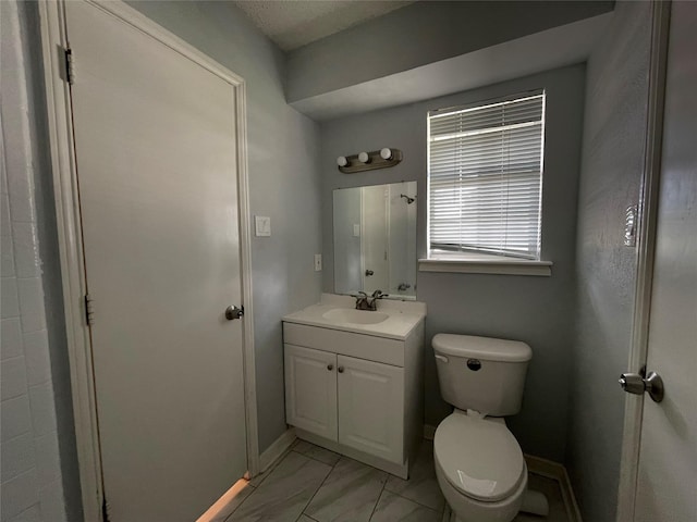 half bathroom featuring marble finish floor, baseboards, vanity, and toilet