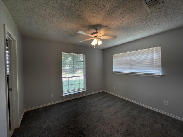 spare room featuring baseboards, visible vents, ceiling fan, dark colored carpet, and a textured ceiling