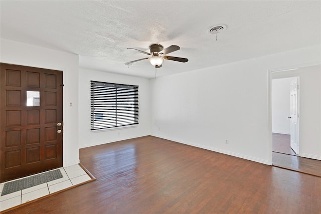 foyer entrance with ceiling fan, a textured ceiling, wood finished floors, visible vents, and baseboards