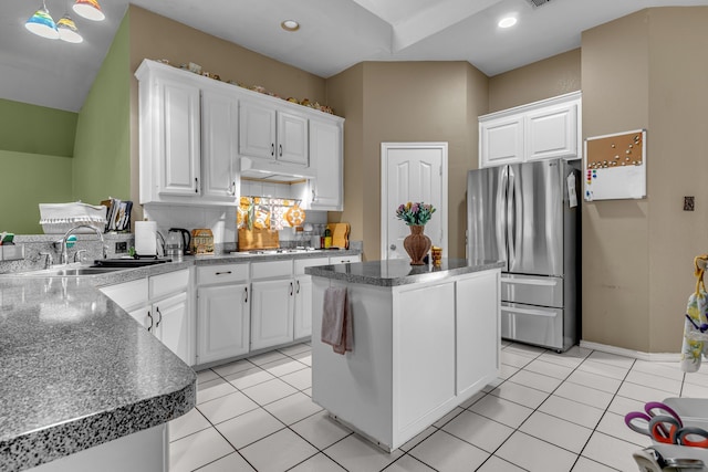 kitchen featuring under cabinet range hood, a sink, white cabinetry, backsplash, and freestanding refrigerator