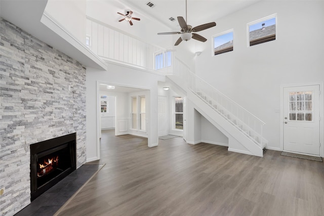 unfurnished living room with a towering ceiling, stairs, wood finished floors, and a stone fireplace