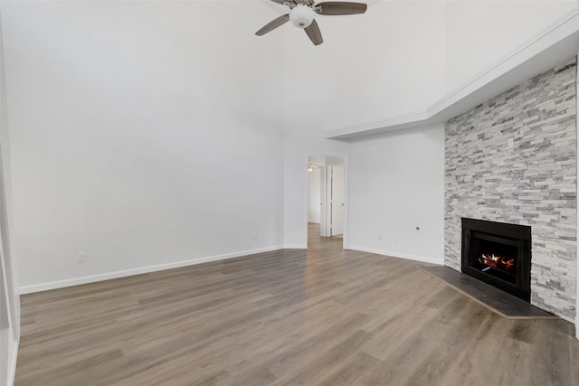 unfurnished living room with ceiling fan, a fireplace, wood finished floors, a towering ceiling, and baseboards