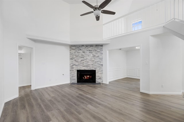 unfurnished living room featuring ceiling fan, a stone fireplace, wood finished floors, and a high ceiling