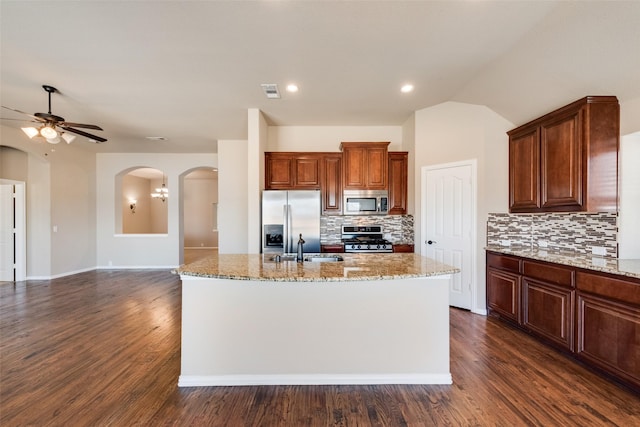 kitchen featuring arched walkways, appliances with stainless steel finishes, dark wood-type flooring, and light stone countertops