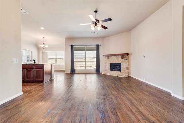 living room featuring dark wood-style floors, ceiling fan with notable chandelier, a fireplace, and baseboards