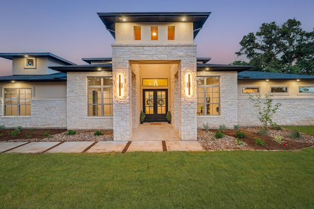 view of exterior entry with french doors, a lawn, and stucco siding