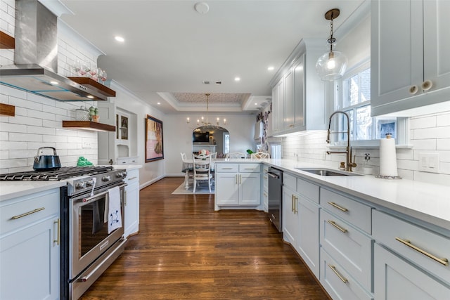 kitchen featuring stainless steel appliances, a sink, wall chimney range hood, open shelves, and a tray ceiling