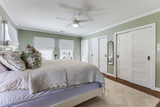 bedroom featuring baseboards, wood finished floors, two closets, and crown molding