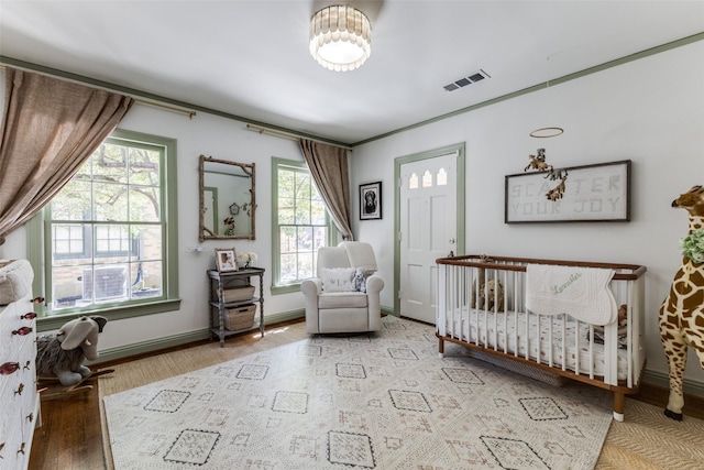 bedroom featuring a crib, baseboards, visible vents, and wood finished floors