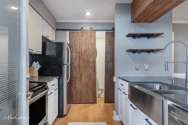 kitchen with white cabinets, dark countertops, stainless steel appliances, light wood-style floors, and a sink