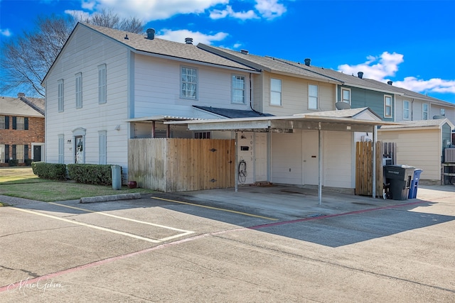 view of front of house featuring uncovered parking, fence, and roof with shingles