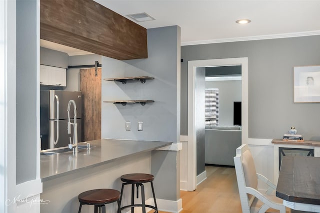 kitchen with a barn door, ornamental molding, freestanding refrigerator, white cabinetry, and a kitchen breakfast bar