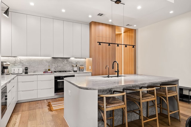 kitchen with wall oven, visible vents, light wood-style flooring, modern cabinets, and a sink