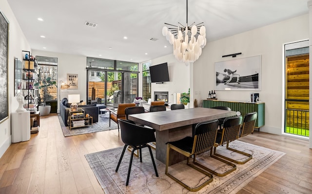 dining area with recessed lighting, visible vents, light wood-style flooring, a glass covered fireplace, and a wall of windows