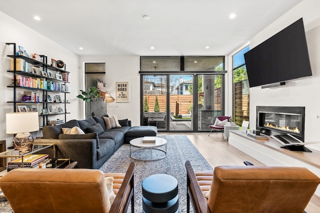 living area featuring a wall of windows, a glass covered fireplace, recessed lighting, and wood finished floors