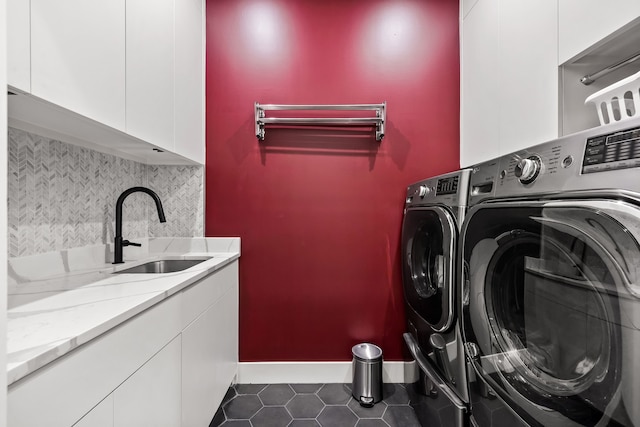 laundry area with cabinet space, washing machine and dryer, a sink, dark tile patterned floors, and baseboards