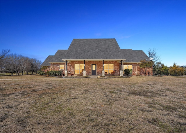 view of front of property with a front yard, brick siding, and roof with shingles