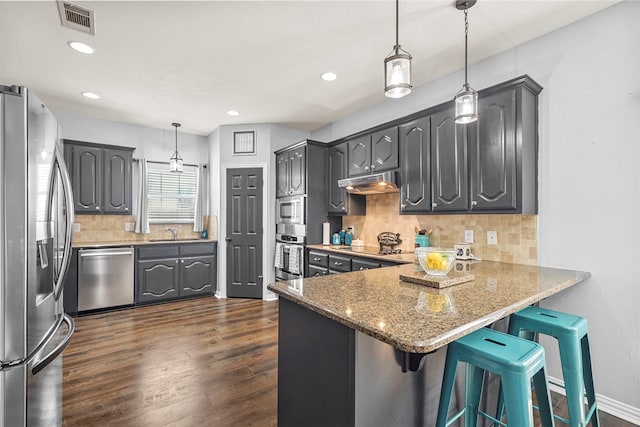 kitchen with under cabinet range hood, a peninsula, dark wood-type flooring, visible vents, and appliances with stainless steel finishes