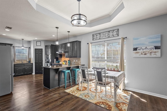 kitchen with a peninsula, freestanding refrigerator, decorative backsplash, a tray ceiling, and dark wood finished floors