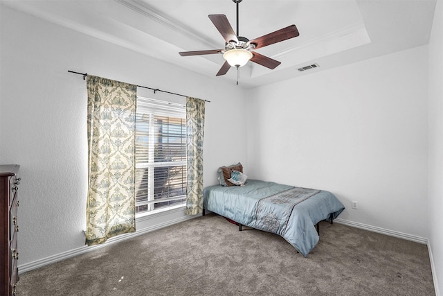 carpeted bedroom featuring a tray ceiling, crown molding, visible vents, a ceiling fan, and baseboards