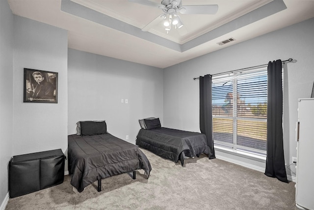 carpeted bedroom with ornamental molding, a tray ceiling, visible vents, and ceiling fan