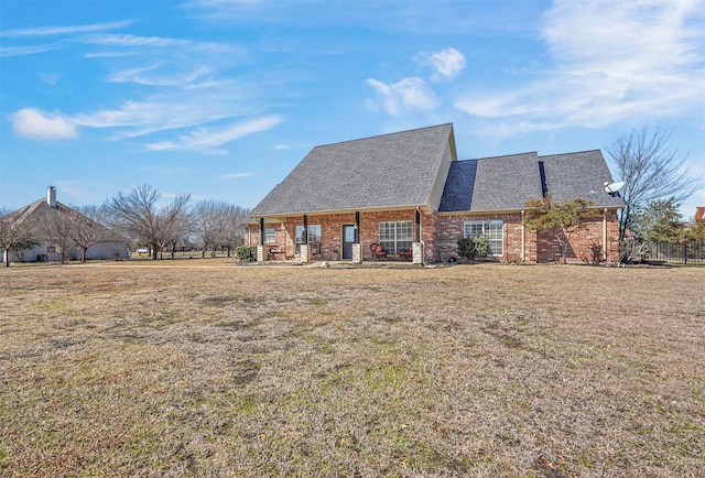 back of house with brick siding, a lawn, and roof with shingles