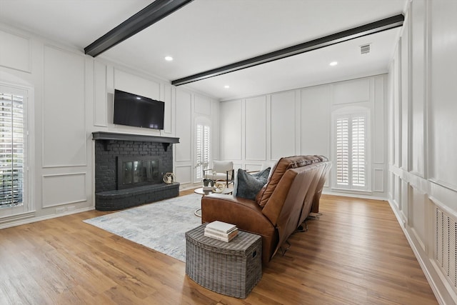 living area with light wood-style flooring, a fireplace, beam ceiling, and a decorative wall