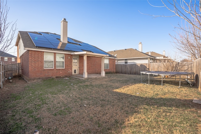 rear view of property with a fenced backyard, brick siding, a lawn, roof mounted solar panels, and a trampoline