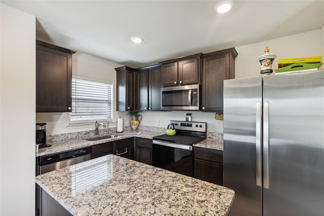 kitchen featuring appliances with stainless steel finishes, light stone counters, a center island, dark brown cabinets, and a sink